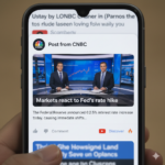 A smartphone screen displaying a Google Discover feed. A prominent card in the feed shows "Post from CNBC" with the CNBC logo, a still image of two news anchors in a studio, and the title "Markets react to Fed's rate hike." Below the image, there's a snippet of text and icons for like, comment, a YouTube Discover button, and a fire icon.